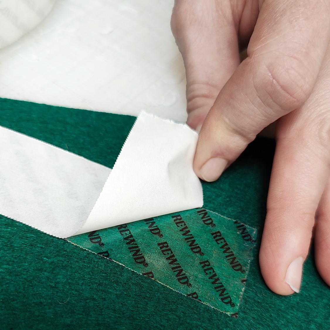 tape bliver klistret fast på bagsiden af gulvtæppe materiale. tapen er gennemsigtig med sort REWIND® logo på
